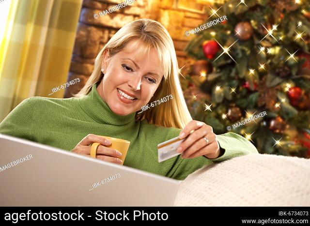Beautiful woman using her credit card in front of christmas tree and laptop computer