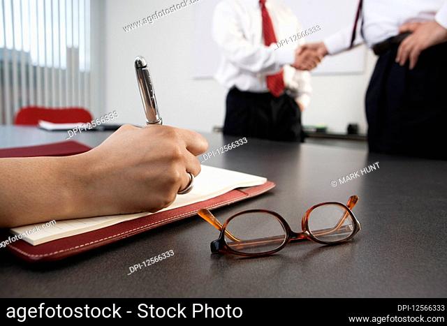Person writing with business men shaking hands in the background