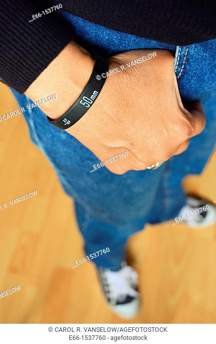 Woman in blue jeans, black sweater and sneakers, wearing a 'Lens Bracelet' designed by Adam Elmakais - with shallow depth of field