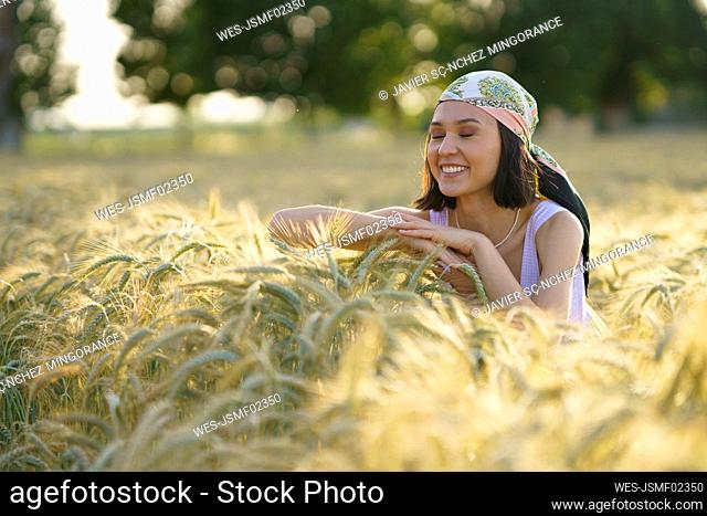Smiling young woman standing with eyes closed enjoying in wheat field