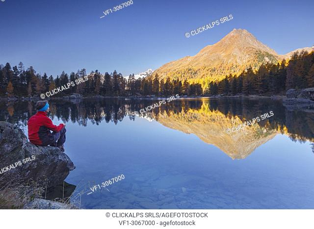 Hiker take a break to admire sunrise on lake Saoseo and Corn da Murasciola mount, Poschiavo, val di Campo, Canton of Graubunden, Switzerland, Europe