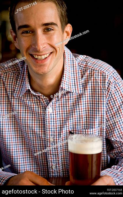 Smiling man sitting and holding a pint of beer