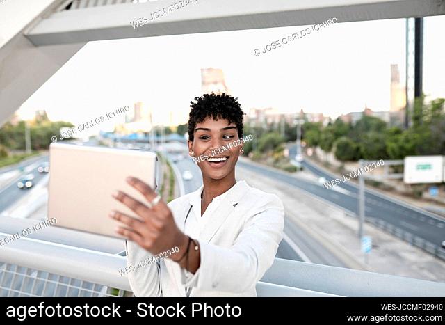 Businesswoman taking selfie through digital tablet on bridge in city