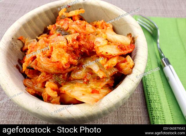 Fermented Napa cabbage with radish and spices recipe prepared and served in a wood bowl. Wooden bowl of spicy and fermented kimchi made of Napa cabbage