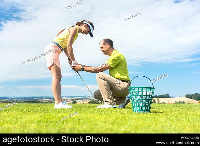 Full length side view of a young woman holding an iron club, while exercising the golf swing helped by her experienced instructor outdoors on green grass