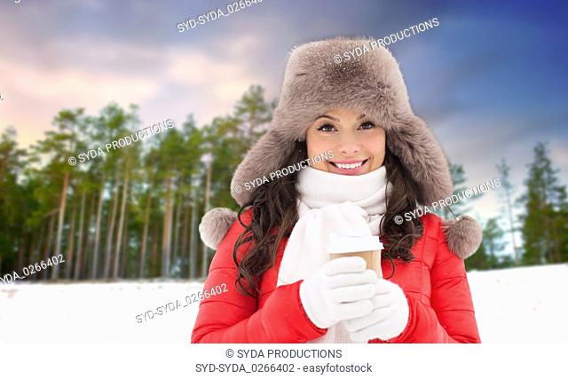 woman in fur hat with coffee over winter forest