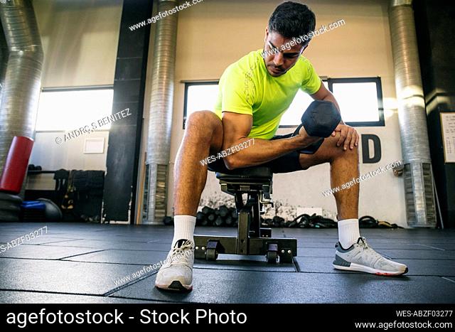 Male athlete lifting dumbbell while sitting in gym