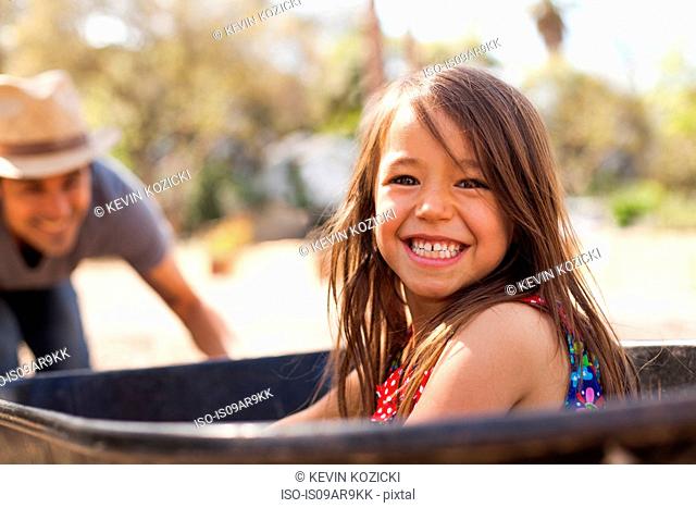 Portrait of girl in community garden riding in wheelbarrow