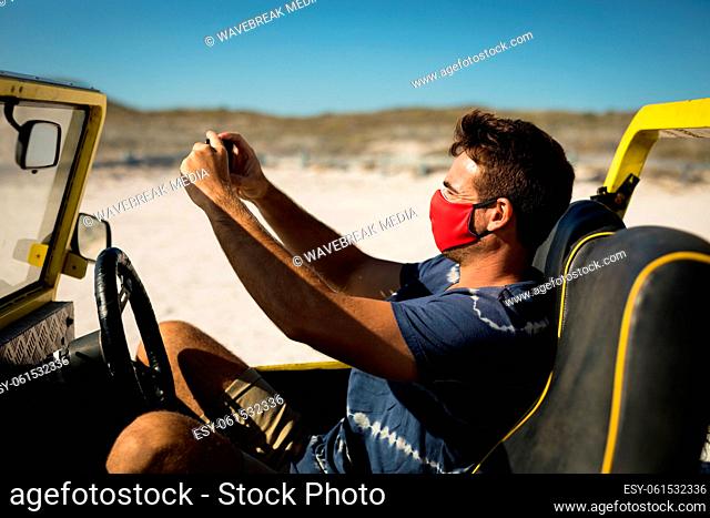 Caucasian man wearing face mask sitting in beach buggy taking picture
