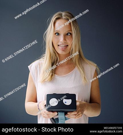 Young woman grimacing holding VR glasses with squinting eyes
