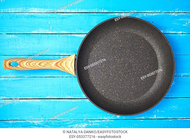 new empty frying pan with a brown handle on a blue wooden background, bottom with a crumb of stone and marble