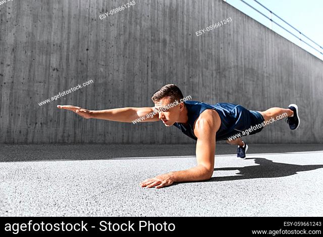 young man doing plank on city street