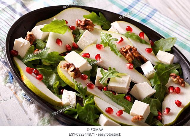Healthy salad with pears, pomegranates, feta cheese, nuts and herbs close up on a plate. horizontal