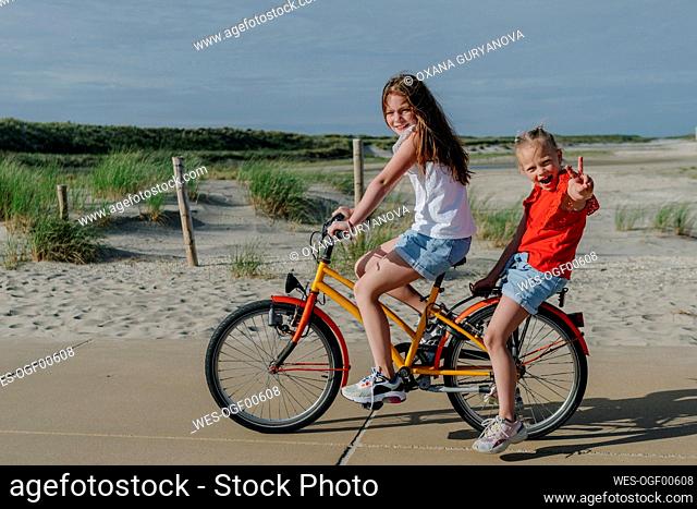 Girl taking younger sibling on bicycle at beach during sunny day