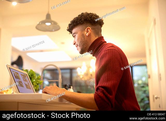 Young man working from home at laptop in kitchen