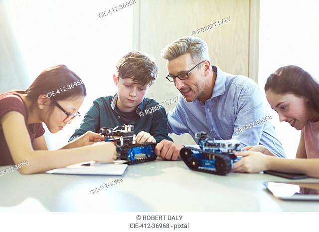 Male teacher helping students assembling robotics in classroom