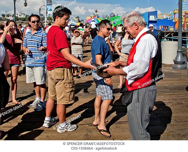 An elderly magician collects contributions in a hat from his audience after a performance in the amusement park on Santa Monica Pier