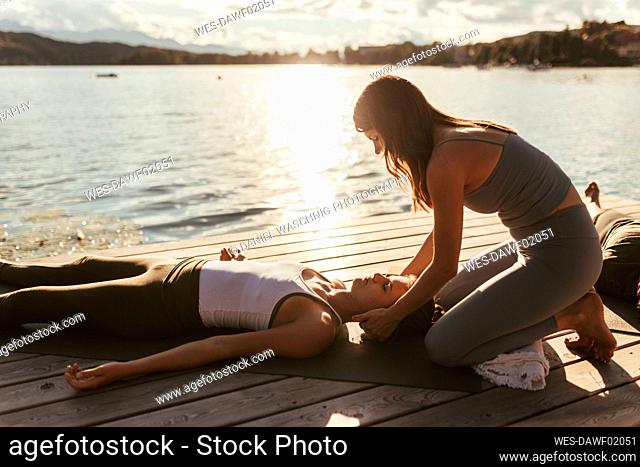 Female instructor assisting women lying down on jetty during yoga class