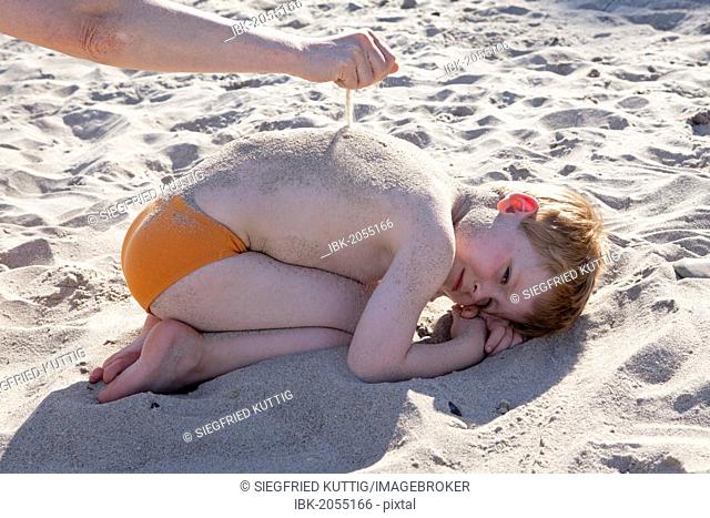 Hand sprinkling sand onto young boy on the beach, Kuehlungsborn, Mecklenburg-Western Pomerania, Germany, Europe