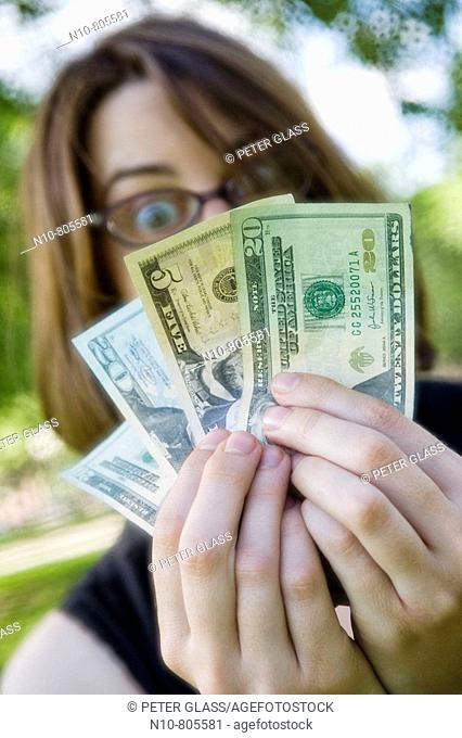 Young woman at a park, wearing glasses and holding up American money