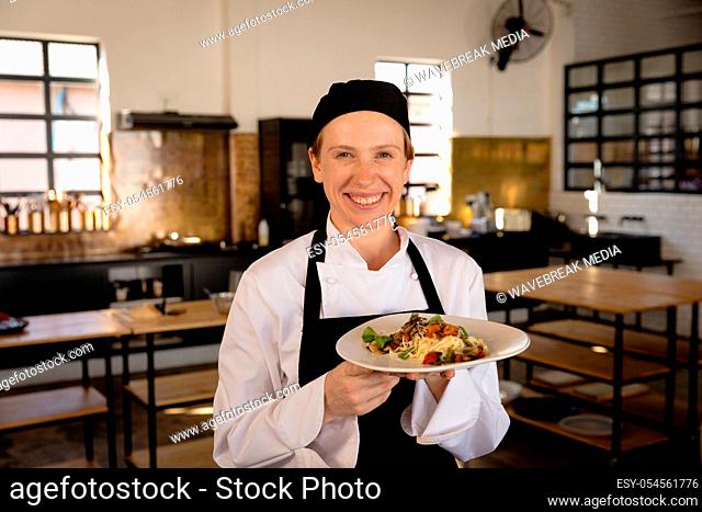 Front view of a Caucasian female chef at a cookery class in a restaurant kitchen, posing holding a prepared fresh pasta dish