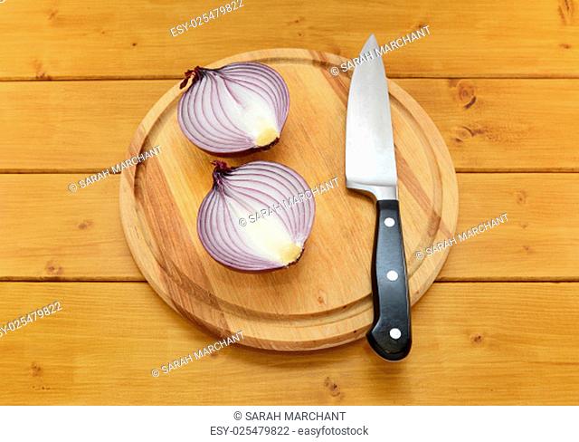 Red onion cut in half with a sharp kitchen knife on a chopping board on a wooden table