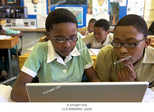 Schoolboy and schoolgirl work on a laptop computer in their classroom, KwaZulu Natal Province, South Africa