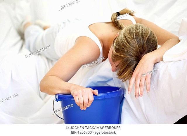 Woman is vomiting into a bucket, nausea, sickness