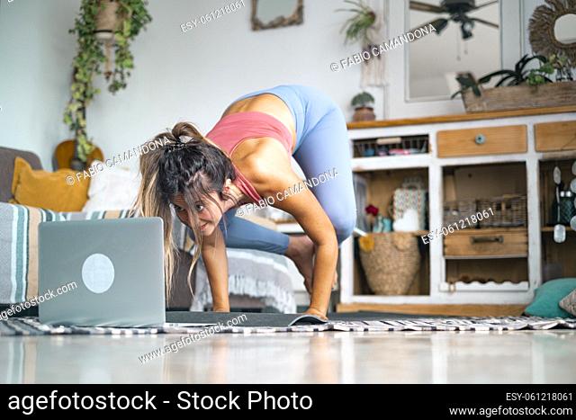 Young woman exercising at home doing push ups and looking at her personal laptop computer to learn or teach workout - content creator business free healthy...
