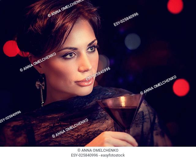 Portrait of beautiful brunet woman on the party, holding in hand glass of martini, spending evening in night club, celebrating New Year