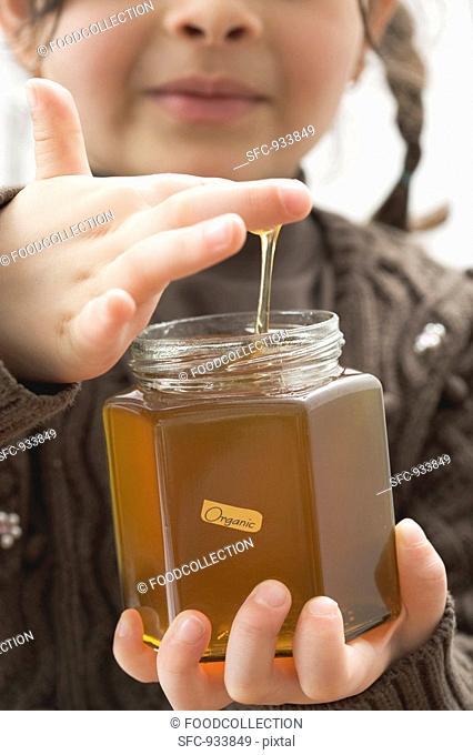 Girl dipping her finger in a jar of organic honey