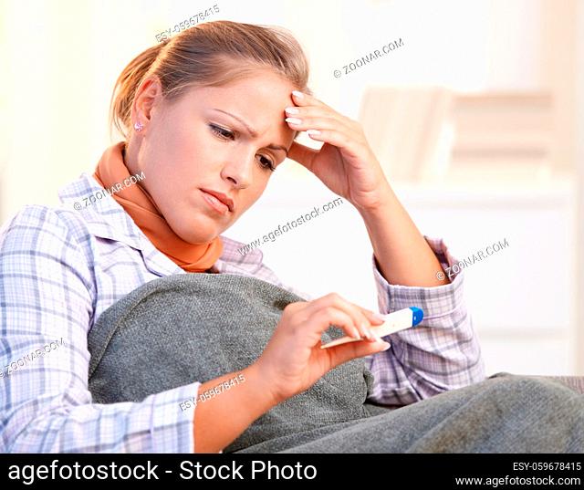 Young woman at home feeling bad, taking her temperature