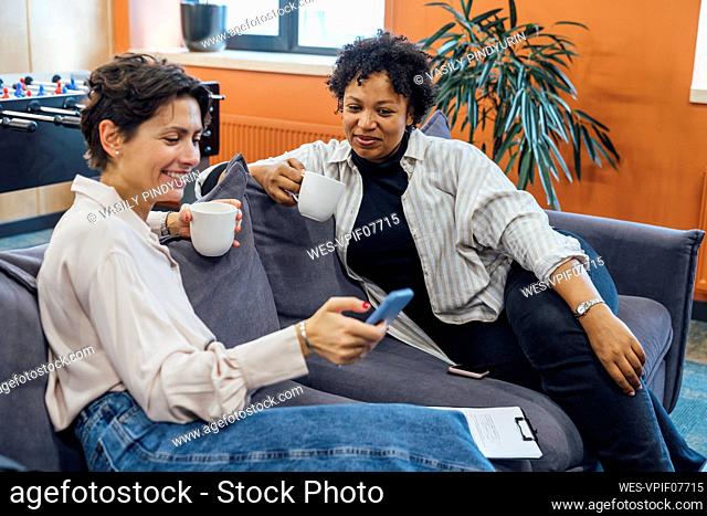 Happy businesswoman using smart phone on sofa at office