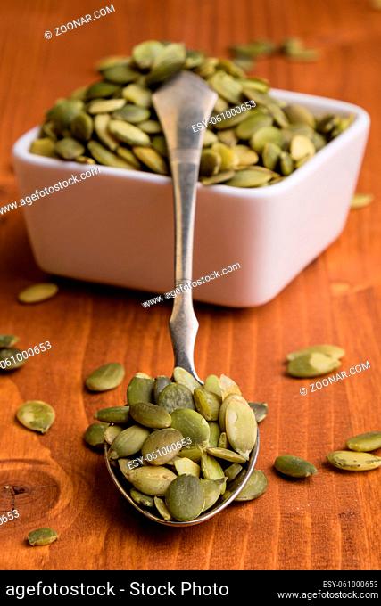 green healthy pumpkin seeds on wooden table with spoon and white bowl