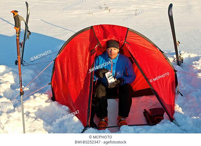 skier sitting in his camp eating freeze-dried food, Sweden, Lapland, Norrbotten, Sarek National Park