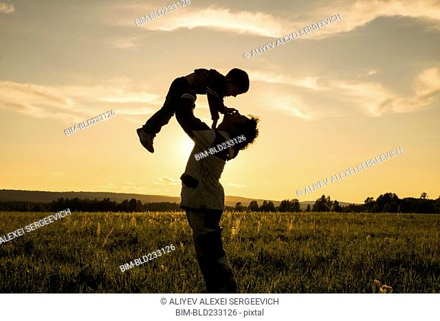 Mari man lifting son in field at sunset