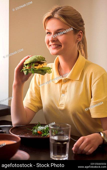 Closeup of lady holding vegan burger in hands while sitting in vegan restaurant or cafe. Hunger, healthy, meal concepts