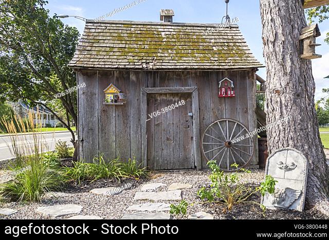 Flagstone footpath in gravel bed leading to old vertical wood plank milk-house with cedar shingles roof covered with green moss in front yard of old home