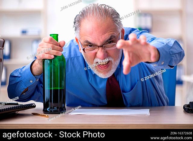 Senior male employee drinking alcohol in the office