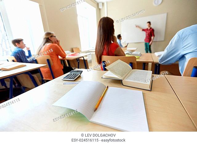 education, high school, learning and people concept - close up of notebook with pencil, book and calculator on desk