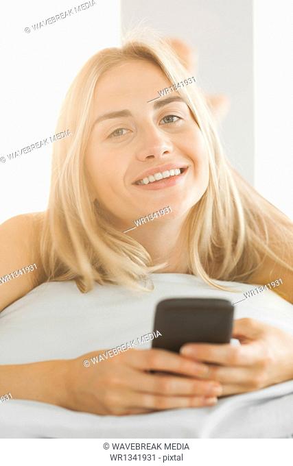 Cheerful blonde lying on her pillow sending a text