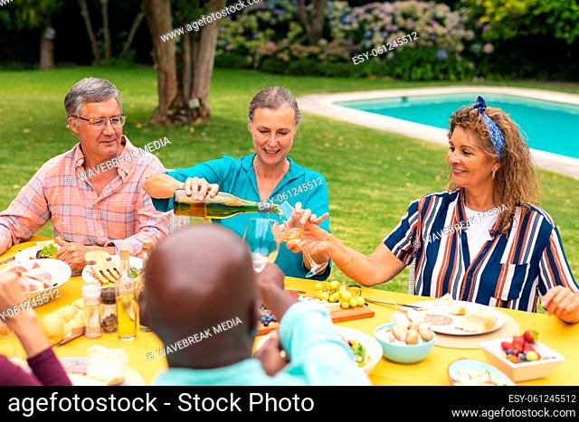 Multiracial senior male and female friends having wine at table during backyard party