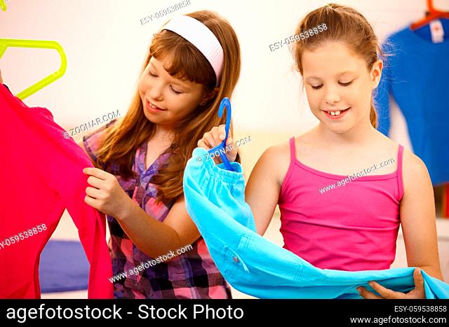 Portrait of girls at home, holding up hanger with clothes, smiling
