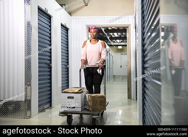 Woman walking down the halls of a storage facility with a cart of boxes