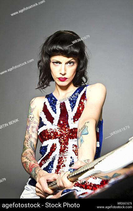 Young woman with guitar and tattoo on her hand against grey background, portrait