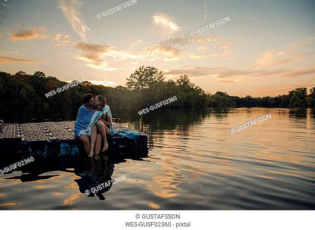 Young couple sitting on bathing platform, kissing, wrapped in towel