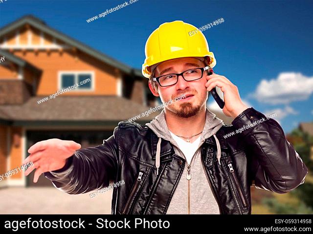 Young Contractor Wearing Hard Hat on Cell Phone In Front of House