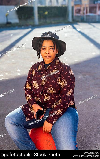 Woman wearing hat holding mobile phone while sitting on footpath