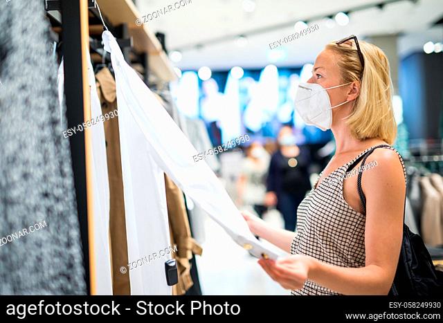 Fashionable woman wearing protective face mask shopping clothes in reopen retail shopping store. New normal lifestyle during corona virus pandemic