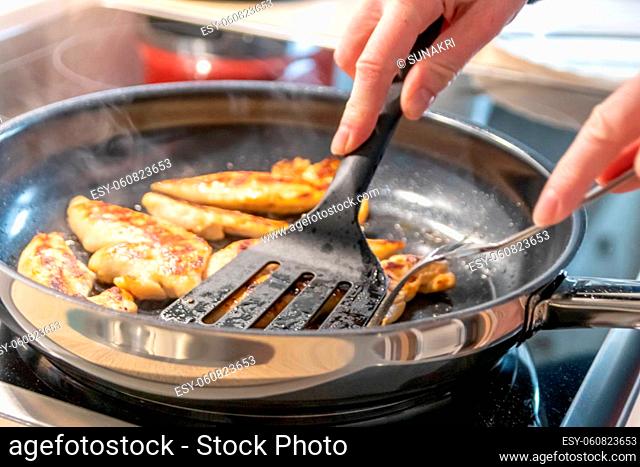 Woman cooking and frying chicken breasts and chicken filet in a pan on an hot stove in the kitchen as delicious meal and diet dinner cuisine for healthy...